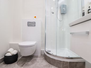 A bathroom with a wall-mounted toilet a shower enclosure and a basket of toilet paper at Sunbury Barn in St Agnes