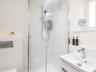 A bathroom with a glass shower enclosure a sink with a faucet a small round mirror and two bottles of soap at Sunbury Barn in St Agnes