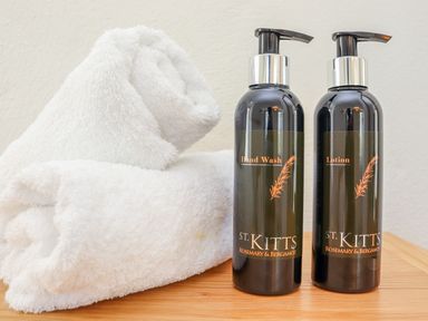 Two black pump bottles of St Kitts hand wash and lotion beside two white rolled towels on a wooden surface