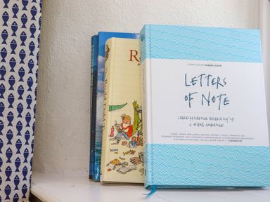 A row of books on a white shelf next to a blue and white patterned curtain