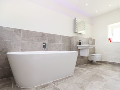 A bathroom with a bathtub sink and toilet with grey tiles at Sunbury Barn in St Agnes
