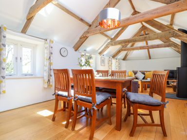 A dining area with a wooden table and six chairs under exposed wooden beams at Sunbury Barn in St Agnes