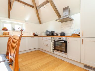 A kitchen with wooden floor wooden chairs built in oven white cabinets and exposed wooden beams at Sunbury Barn in St Agnes