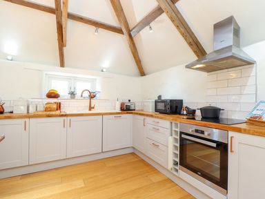 A kitchen with white cabinets wooden countertops and exposed wooden beams at Sunbury Barn in St Agnes