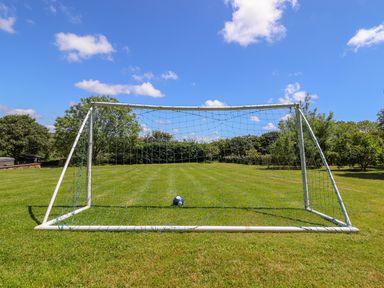 A soccer goal with a ball on grass in a field with trees and blue sky at Sunbury Barn in St Agnes
