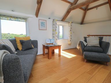 A living room with gray sofa and armchair wooden table and exposed wooden beams at Sunbury Barn in St Agnes