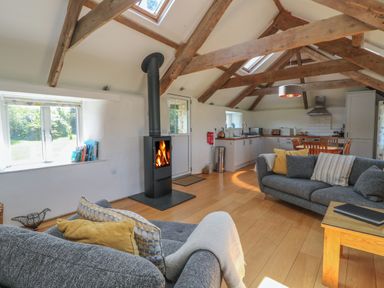 An open plan living room and kitchen with exposed wooden beams and a wood burning stove at Sunbury Barn in St Agnes