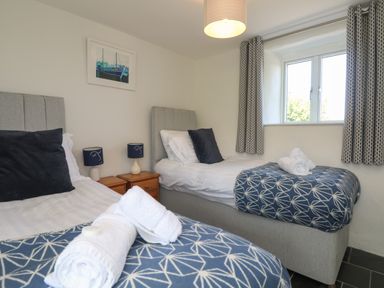 A bedroom with two single beds side by side with towels on top and a window with patterned curtains at Sunbury Barn in St Agnes