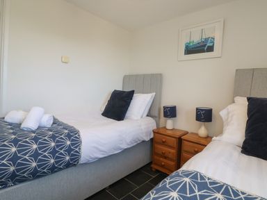 A bedroom with two single beds a wooden nightstand and a framed picture of boats at Sunbury Barn in St Agnes