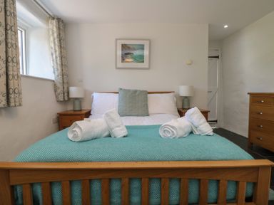 A bedroom with a wooden bed frame a teal blanket two bedside tables with lamps and a chest of drawers at Sunbury Barn in St Agnes