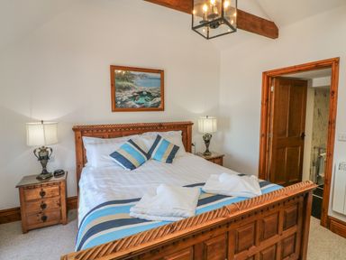 A bedroom with a wooden bed frame side tables lamps and a painting on the wall at C S Lewis Balcony in Lynton