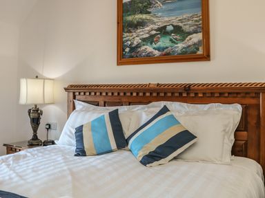 A bed with wooden headboard striped pillows and white bedding with a lamp on a bedside table at C S Lewis Balcony in Lynton