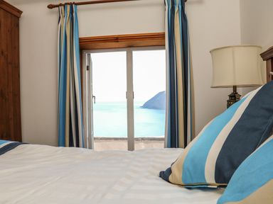 A bedroom with blue striped pillows on a bed next to a window with blue striped curtains showing a sea view at C S Lewis Balcony in Lynton