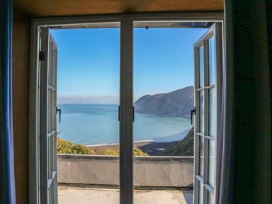 An open window looking out to a balcony with a view of the ocean and cliffs at C S Lewis Balcony in Lynton