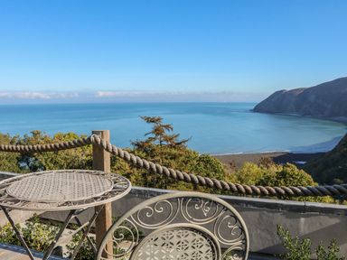A balcony with a metal table and chair overlooking the sea and cliffs at C S Lewis Balcony in Lynton