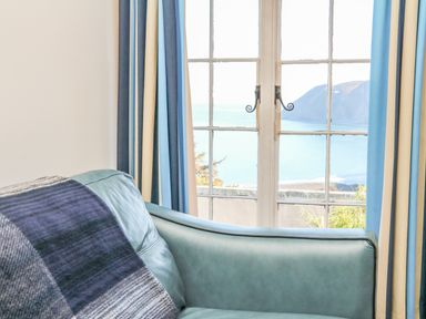 A blue leather sofa near windows with blue and cream curtains overlooking the sea at C S Lewis Balcony in Lynton