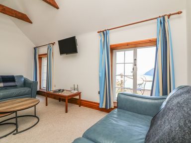 A sitting room with blue sofas a wall-mounted tv blue and white curtains and a wooden coffee table at C S Lewis Balcony in Lynton