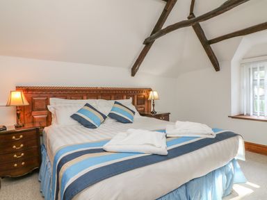 A bedroom with a large bed with striped pillows and blankets with wooden headboard and bedside tables with lamps at C S Lewis Balcony in Lynton