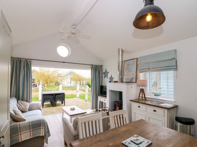 An open plan living and dining area with sofas a dining table a coffee table a wood burning stove and a deck with outdoor furniture at Sea Breeze The Bay near Filey
