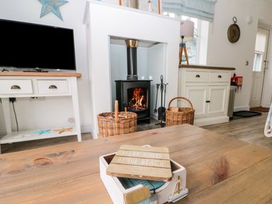 A living room with a wood-burning stove two wicker baskets a wooden table with a decorative box and a TV on a white stand at Sea Breeze The Bay near Filey