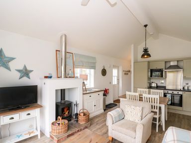 An open living room and kitchen area with a wood-burning stove a dining table and chairs a TV on a stand and a beige armchair at Sea Breeze The Bay near Filey