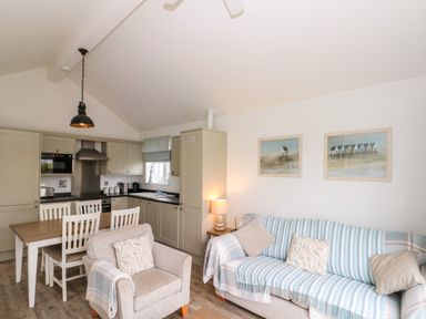 A kitchen with dining table and chairs next to a living area with armchair and sofa at Sea Breeze in The Bay near Filey