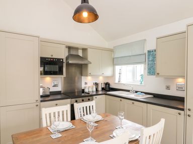 A kitchen with beige cabinets black countertops a wooden dining table set for four and a window with a light blue blind at Sea Breeze The Bay near Filey
