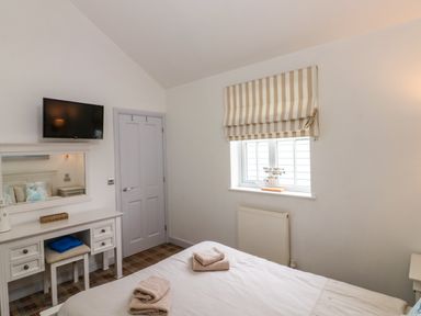 A bedroom with a bed with folded towels a window with striped blinds a vanity table with a mirror and a wall mounted television at Sea Breeze in The Bay near Filey