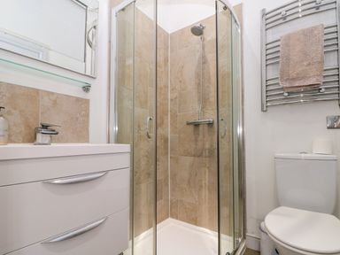 A bathroom with a corner shower with glass doors a white vanity cabinet with a sink a toilet and a towel rack with a towel at Sea Breeze The Bay near Filey
