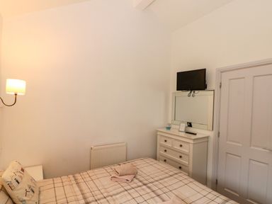 A bedroom with a bed with folded towels a chest of drawers with a mirror and a TV mounted above at Sea Breeze The Bay near Filey