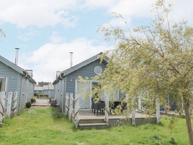 A pair of blue wooden cottages with chimneys a small deck with chairs and a tree in the grass between cottages at Sea Breeze The Bay near Filey
