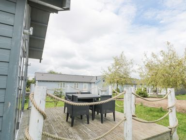 An outdoor wooden deck with a table and chairs surrounded by rope fencing and trees at Sea Breeze The Bay near Filey