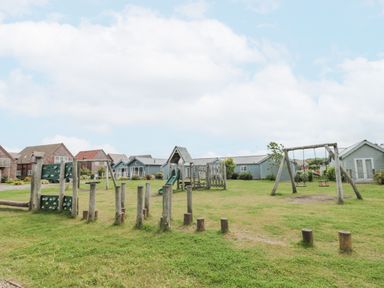 A playground with wooden play structures and swings near blue houses at Sea Breeze in The Bay near Filey