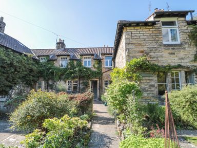 A stone cottage with tiled roof and garden pathway surrounded by plants and bushes at Teviot Cottage in Corbridge