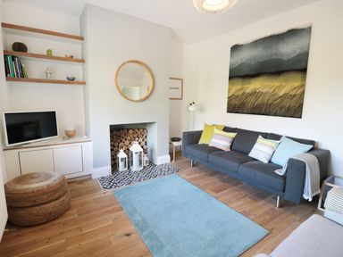 A living room with a gray sofa and colorful cushions a blue rug a wall mirror and a TV at Teviot Cottage in Corbridge