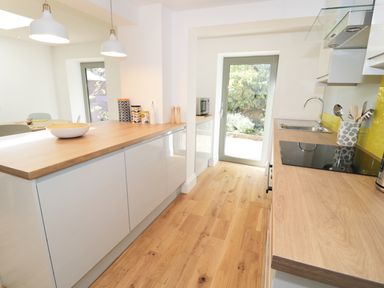 A kitchen with wooden countertops white cabinets wooden floor and glass door to garden at Teviot Cottage in Corbridge