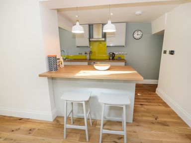 A kitchen with a wooden countertop and two white stools at Teviot Cottage in Corbridge