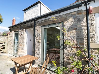 A stone exterior wall with glass doors and wooden table and chairs outside at Teviot Cottage in Corbridge