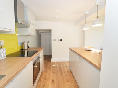 A kitchen with wooden countertops white cabinets a yellow backsplash and pendant lights at Teviot Cottage in Corbridge