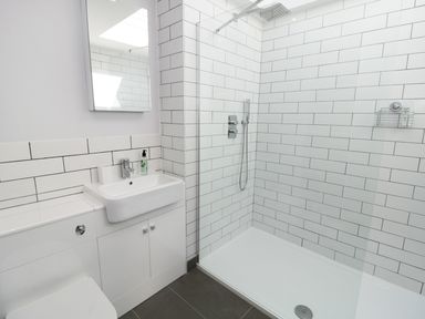A bathroom with a sink, mirror, toilet, and shower area with white tiled walls at Teviot Cottage in Corbridge
