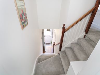 A stairway with grey carpet and wooden handrail leading down to a doorway with a poster on the wall at Teviot Cottage in Corbridge