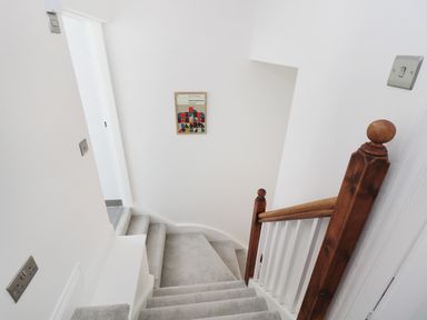 A carpeted staircase with wooden handrail and white walls with a colorful framed picture on the wall at Teviot Cottage in Corbridge
