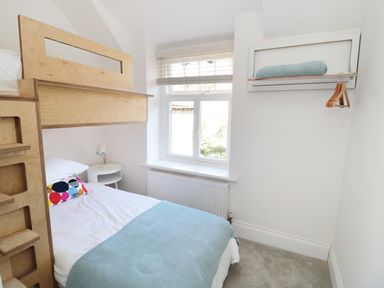 A bedroom with a bunk bed, a window, a small white bedside table, and a wall-mounted shelf with hangers and a folded blanket at Teviot Cottage in Corbridge