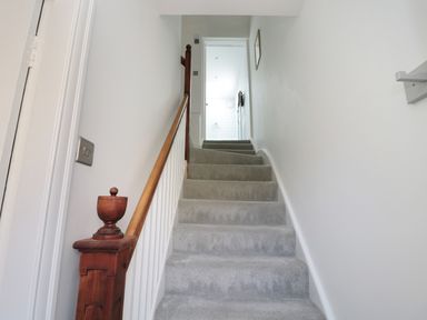 A carpeted staircase with wooden handrail and white walls leading to a hallway with a door at Teviot Cottage in Corbridge