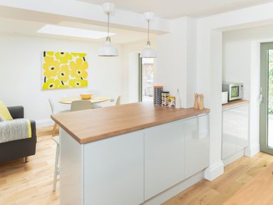 A kitchen with wooden countertops white cabinets pendant lights and a dining area with a round table and yellow floral wall art at Teviot Cottage in Corbridge