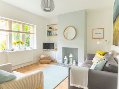 A living room with a gray sofa with pillows a beige armchair a blue rug a small television and sunflowers on a windowsill at Teviot Cottage in Corbridge