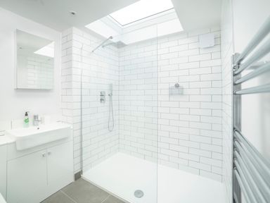 A bathroom with a walk-in shower, white tiled walls, a sink with cabinet, a mirror, and a heated towel rail at Teviot Cottage in Corbridge