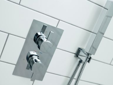 A close up of shower controls and a handheld showerhead on white tiled wall at Teviot Cottage in Corbridge