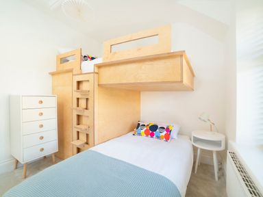 A bedroom with a wooden bunk bed colorful pillow white chest of drawers and a white bedside table with a lamp at Teviot Cottage in Corbridge
