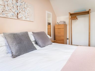 A bedroom with a bed with two gray cushions a chest of drawers and a wooden clothes rack at Teviot Cottage in Corbridge